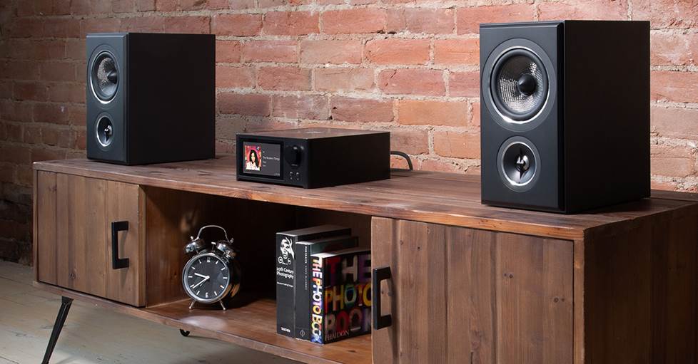 Integrated amplifier and bookshelf speakers on a wooden shelf in a modern living room