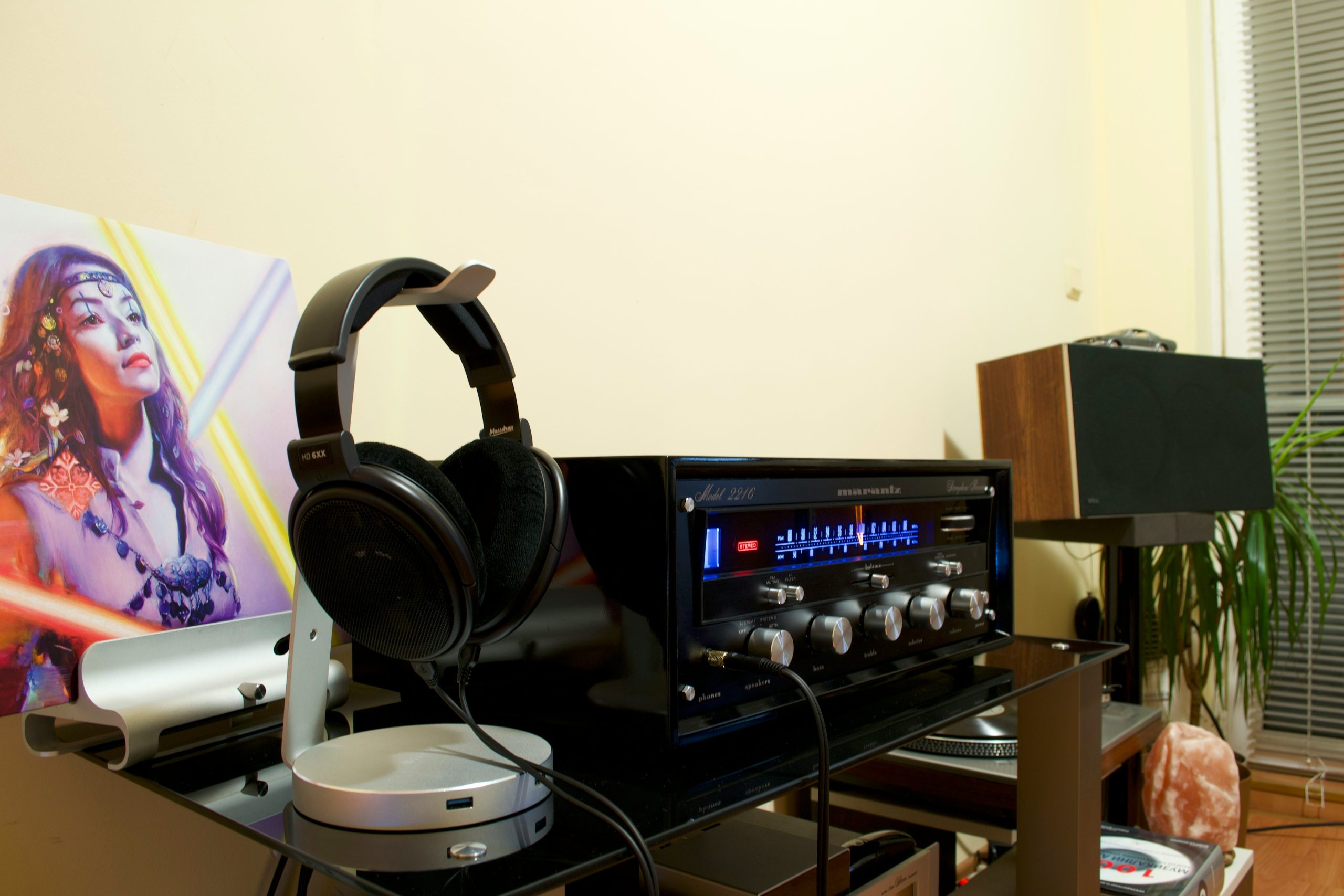 Classic Hifi Setup A classic Marantz Model 2216 stereo receiver with illuminated blue tuning and signal meters on a black shelf, next to a pair of open-back Sennheiser HD 6XX series headphones on a silver stand.