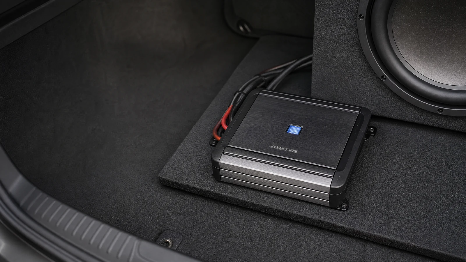 Alpine MRV-M500 mono car amplifier beside a subwoofer enclosure in a realistic trunk installation