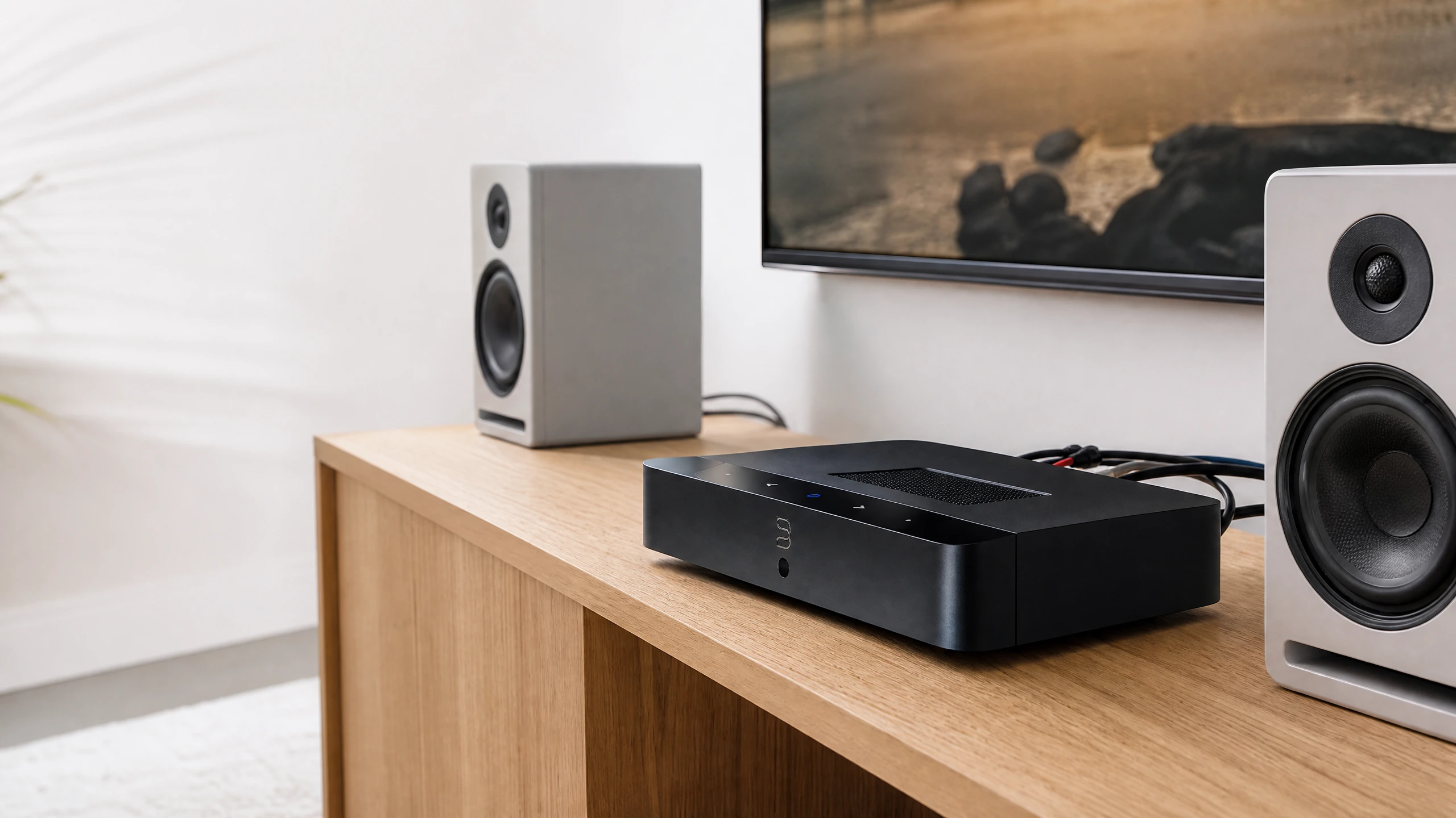 Black Bluesound POWERNODE EDGE streaming amplifier on a light oak console between bookshelf speakers and a television