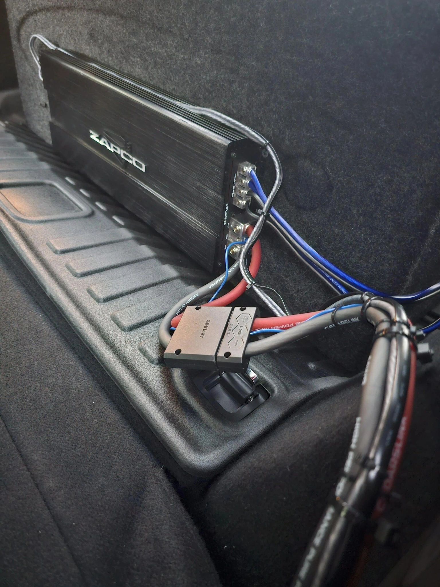 Car amplifier wiring kit installed with cables routed through firewall