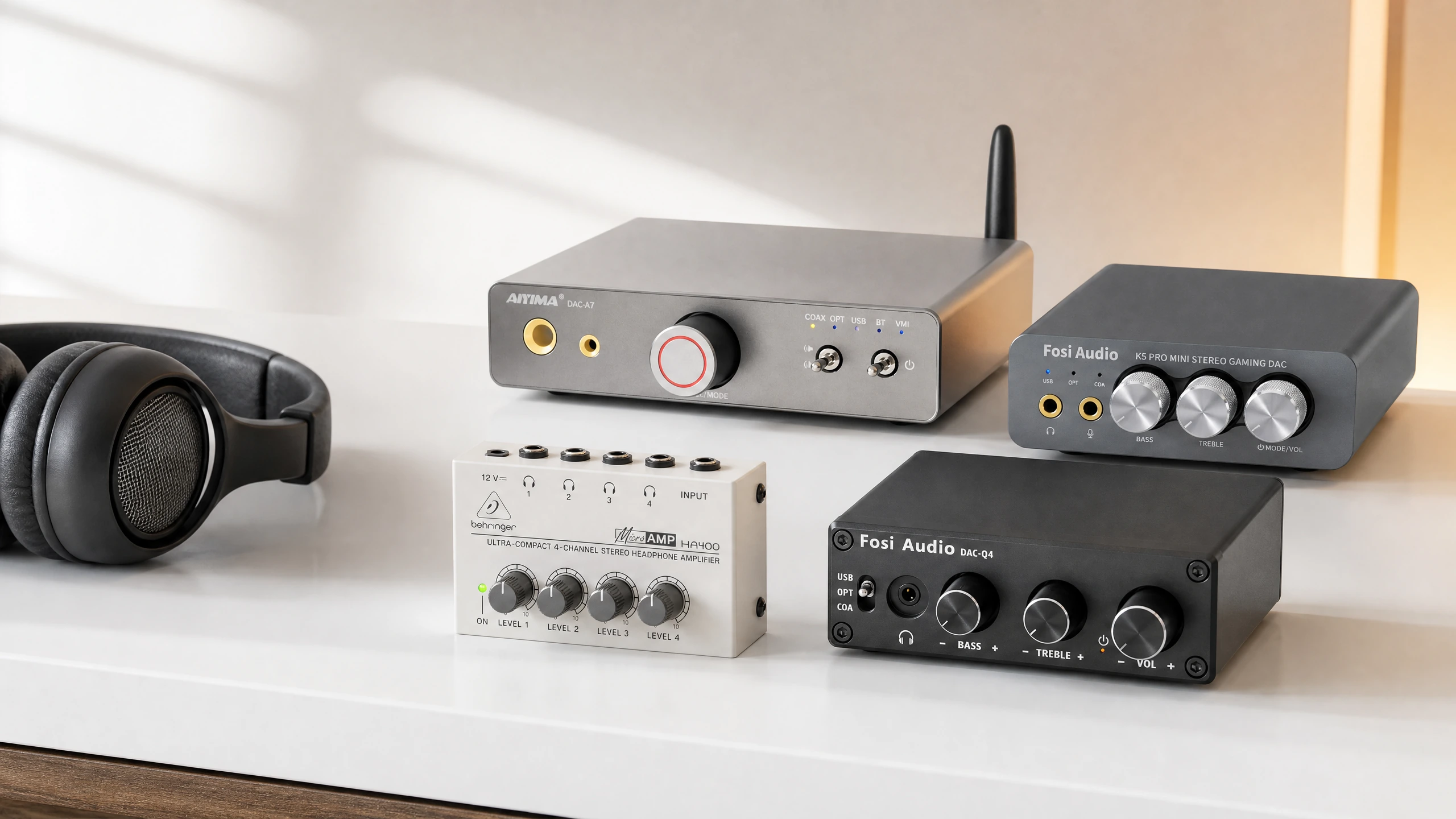 Four compact headphone amplifiers arranged on a clean desktop beside over-ear headphones